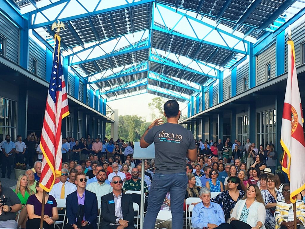 Fracture co-founder speaking at a Tech City event, addressing a large audience under a solar-paneled pavilion