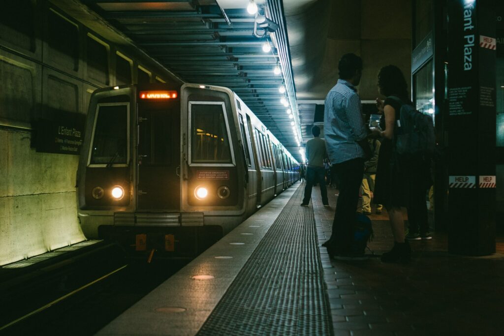 People waiting at night as a subway train arrives, with two individuals engaged in conversation