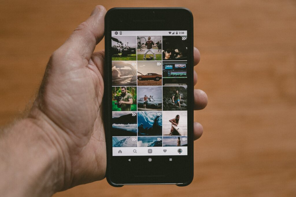 Hand holding a smartphone displaying a grid of photos on a social media app