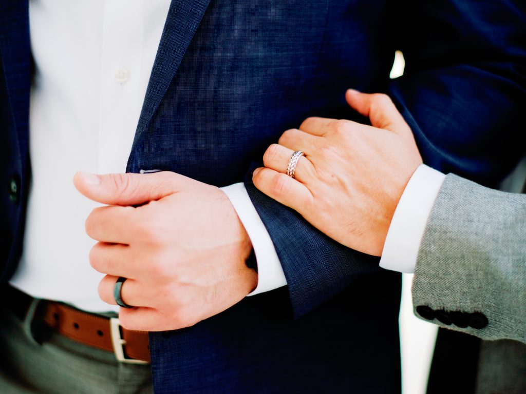 Groom and groomsman clasping arms, highlighting their wedding rings, a close-up capturing the intimate bond 