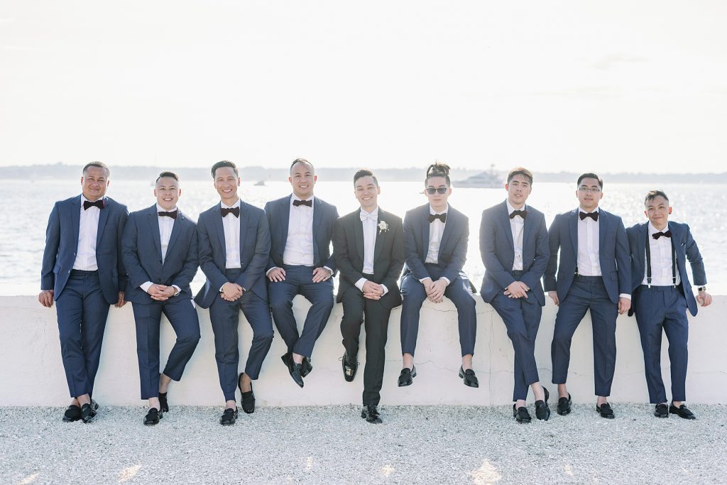 Groom and groomsmen in navy suits posing by the waterfront, capturing a memorable moment for the wedding album