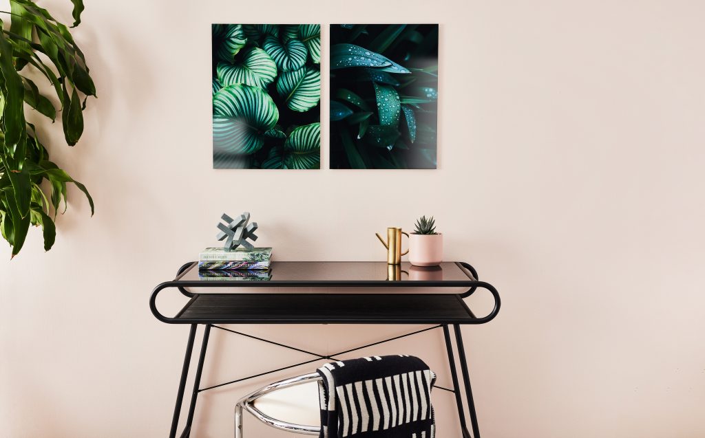 Table with home decor accessories and beige wall with glass prints of plants