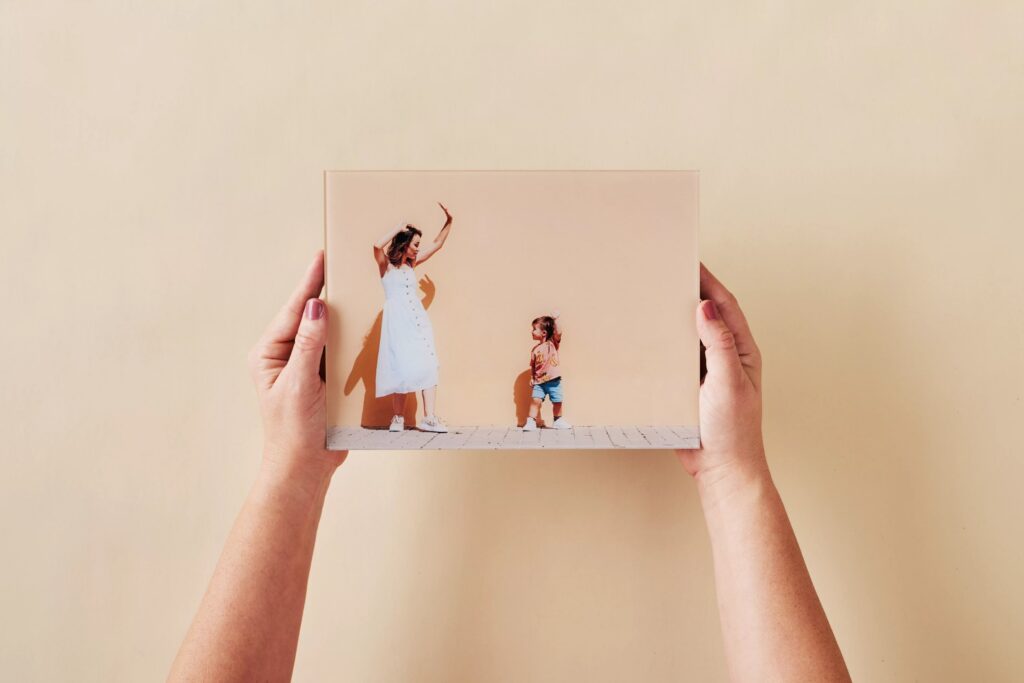 Hands holding a Mother's Day photo gift printed on glass, featuring a mom and her toddler striking a pose in front of a colorful wall.