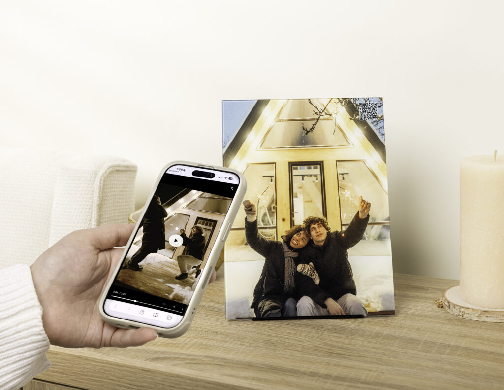 A StoryGlass custom glass print with a subtle QR code in the corner reveals the video of the memory—a surprise proposal in front of a charming, snowy a-frame.