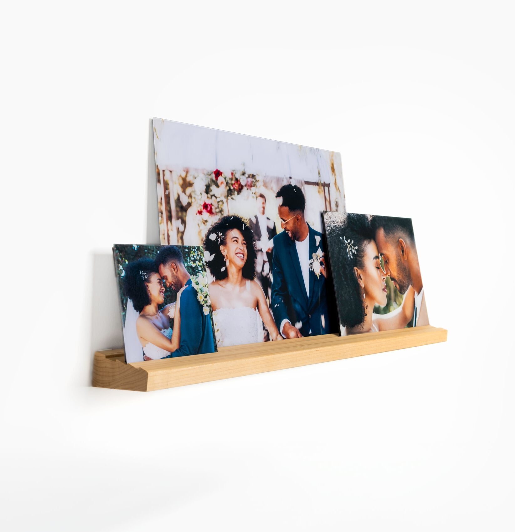 A trio of wedding photos printed beautifully on frameless glass are displayed on a floating wall shelf.