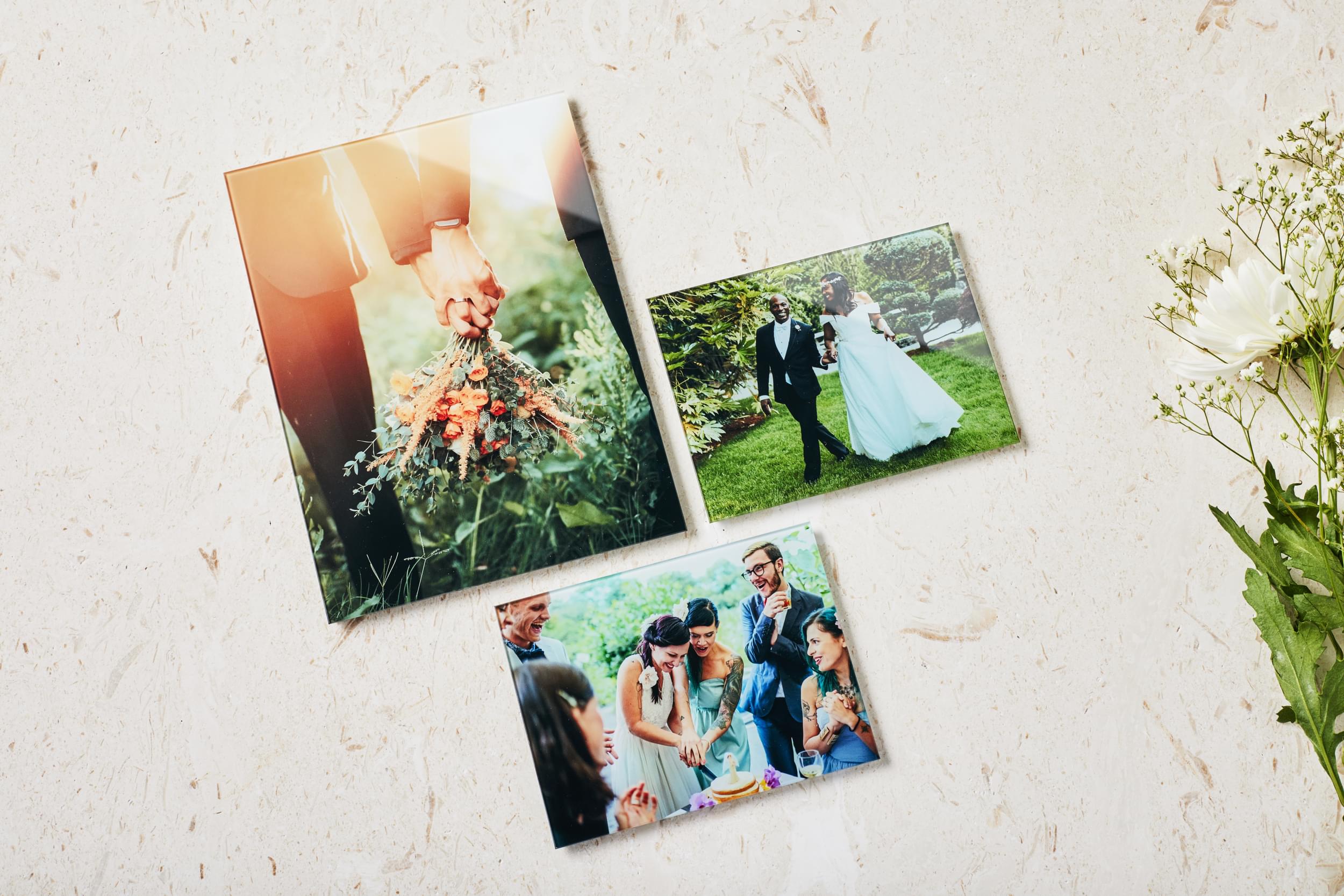 The best gifts for the couple that has everything: a trio of wedding photos printed on glass sits on a limestone backdrop with a bouquet of white flowers peeking out from the side.
