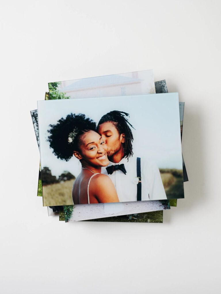 What to do with your wedding photos after you print them: display ideas, gallery walls, and glass prints. A stack of wedding photos printed on glass sits artistically in a pile on a white background.