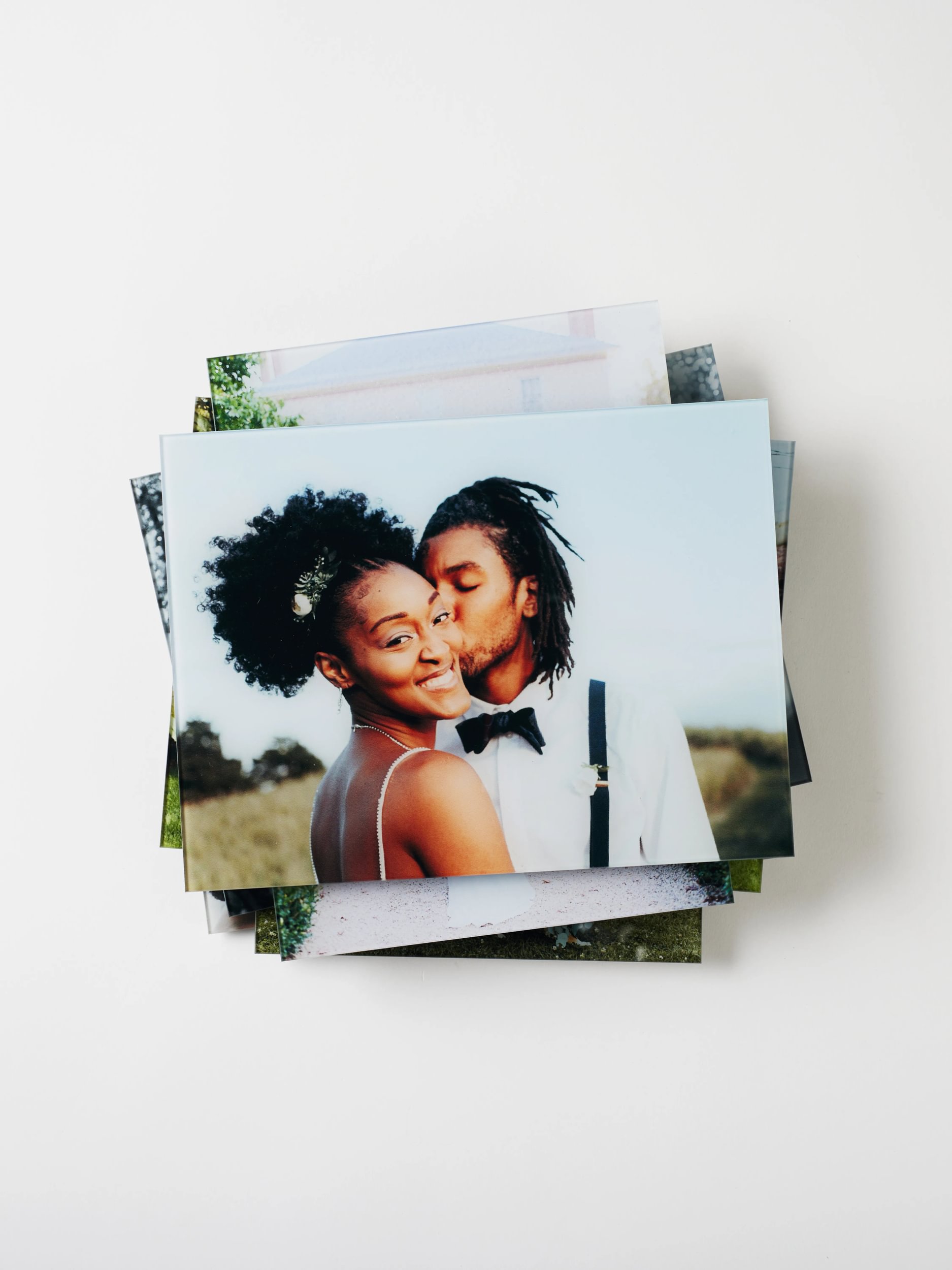 What to do with your wedding photos after you print them: display ideas, gallery walls, and glass prints. A stack of wedding photos printed on glass sits artistically in a pile on a white background.