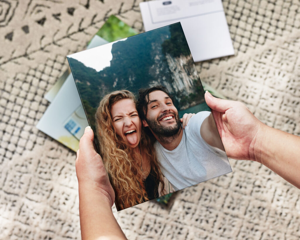 Someone holds a beautifully printed glass print of a travel photo with a goofy selfie showing off the couple's personality, given as a glass anniversary gift.